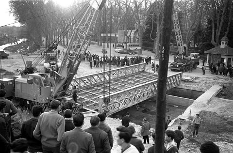 Obres de desmuntatge i trasllat del pont del Rellotge, sobre el riu Güell. Grues aixecant l'estructura en l'emplaçament original a la Devesa, al costat de la Casa del Rellotge. Març 1963