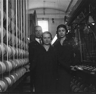 Interiors de la fàbrica Grober. Retrat d'un home i dos dones entre les màquines.
