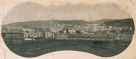 Vista de la ciutat des de l'eixample. En primer terme a la dreta, el convent de les Adoratrius. En segon terme, el tram de la muralla del Mercadal comprès entre el baluard de Santa Clara i la plaça Calvet i Rubalcaba. Al centre, l'Hospital de Santa Caterina. 1896-1905