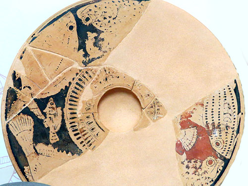 Plat de peix de ceràmica àtica de figures roges. La cassoleta del fons servia per recollir l'oli o posar-hi alguna salsa. S'hi representen dues parelles de peixos de roca, propis de l'àrea mediterrània, encarades dos a dos: una escópora amb un moll, i una escórpora ab un sard, la part posterior d'un anfós, un altre peix no identificat i una vieira. El plat, que té una cronologia pròpia del segle IV aC, es va trobar en una casa de finals del segle III aC, fet que remarca el valor que es va atorgar a aquesta peça