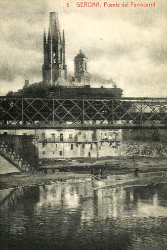 El pont del Ferrocarril, sobre el riu Onyar, a l'altura del portal de la Barca. Al fons, els campanars de l'església de Sant Feliu i de la Catedral de Girona. 1900-1930