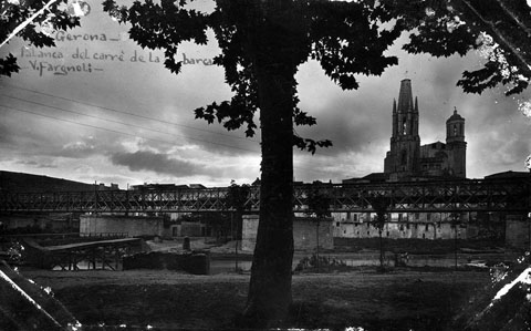 Vista del riu Onyar a l'altura del pont del Ferrocarril, en segon terme. A l'esquerra, la palanca del carrer del portal de la Barca. Al fons sobresurten el campanar de l'Església de Sant Feliu i la Catedral de Girona. 1920-1930