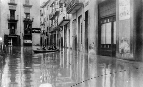 Plaça del Mercadal inundada. Dos homes en una piragua naveguen per la plaça. 1940