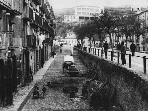 La plaça de Sant Pere. En primer terme es veuen els estris d'un carreter que realitza la seva activitat al carrer. Al fons, l'escola Ignasi Iglésias, a la muntanya de Montjuïc. 1932-1934