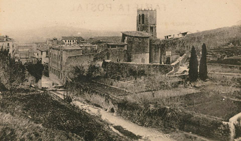 Vista del monestir de Sant Pere de Galligants i del tram de muralla que enfila cap a Montjuïc. En primer terme, el llit del riu Galligants. Al centre, adossat a la muralla, el tambor de Sant Daniel i el portal de Sant Pere. 1896-1911