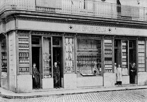 Façana i aparadors de la farmàcia Roca, a la plaça de l'Oli, amb els empleats a les portes d'entrada. 1925-1935