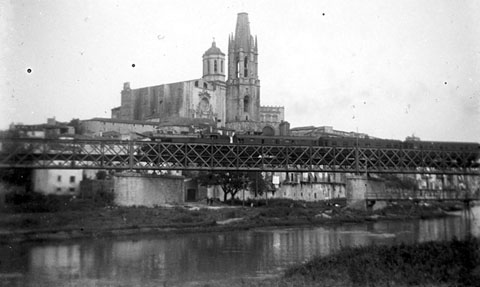 Pont del Ferrocarril sobre el riu Onyar amb un tren circulant. Sota el pont, a la dreta, la passera del Portal de la Barca. 1930-1935