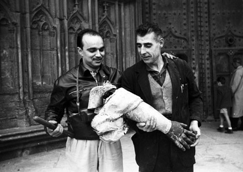Desmuntatge de l'Àngel de la Catedral. Retrat del fotògraf Josep Buil Mayral amb un dels cosins Rueda davant la porta dels Apòstols amb un dels braços de l'àngel retirat. 1960