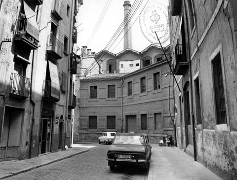 Vista del carrer del Perill, amb una de les xemeneies de la Grober al fons. 1974