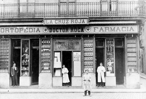 Establiment Ortopèdia-farmàcia Doctor Roca. A la façana de l'establiment hi apareix el rètol de la farmàcia i el de l'administració de loteria n 2
