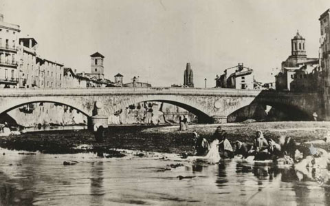 Dones rentant la roba al riu Onyar, davant del pont de Pedra. Al fons, el campanar de Sant Feliu. 1870-1873